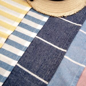 A collection of colorful striped beach towels with a sun hat on top, perfect for summer leisure.